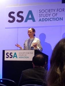 Olivia Maynard presenting behind a podium at the Society for the Study of Addiction 2025 conference